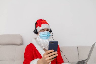 Noel Baba gibi giyinmiş, kulaklık takmış, dizüstü bilgisayarlı bir adam.