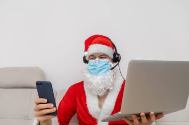 Noel Baba gibi giyinmiş, kulaklık takmış, dizüstü bilgisayarlı bir adam.