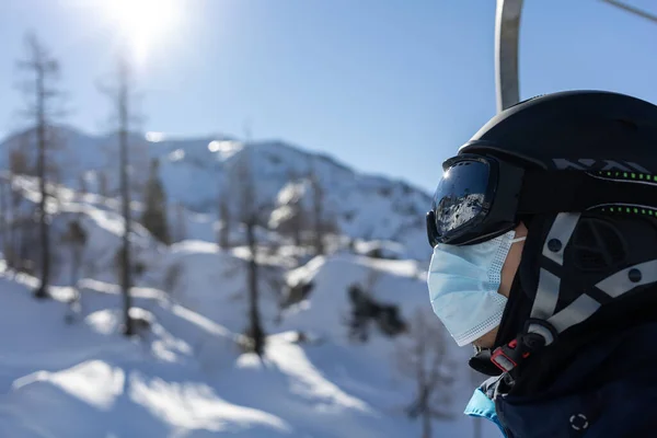 Station de ski homme sur télésiège en casque et masque médical — Photo