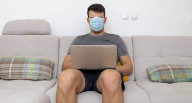 mask covering whole face man with laptop on sofa. High quality photo
