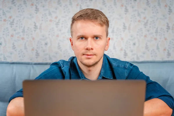 若い男がテーブルに座ってノートパソコンの下から外を見ている 自宅やカフェからリモートでノートパソコンで作業します テクノロジー リモートワーク ソーシャルネットワーク — ストック写真