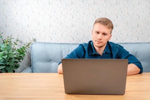 若い男がテーブルに座ってノートパソコンの下から外を見ている 自宅やカフェからリモートでノートパソコンで作業します テクノロジー リモートワーク ソーシャルネットワーク — ストック写真