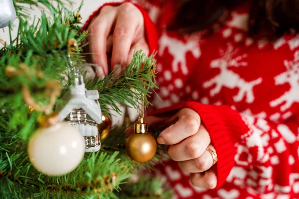 一位穿着红色毛衣的年轻女子在家里的树上挂着圣诞玩具 — 图库照片