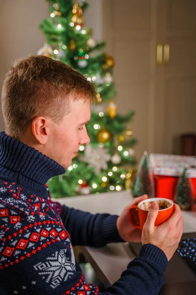 お祝いのセーターの男は お正月とクリスマスの間にマシュマロとココアを飲みます 自宅や職場での休日の美しい雰囲気 — ストック写真