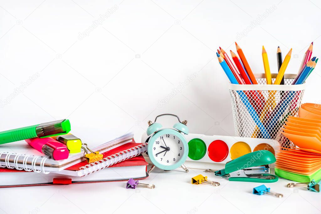 A table for a school with colored stationery, paints, an alarm clock on a white background. Back to school concept.