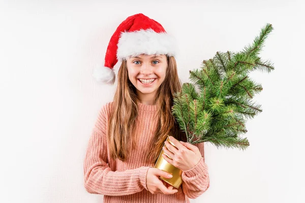 크리스마스 모자를 아름다운 금발의 소녀가 웃으며 배경에 크리스마스 트리를 있습니다 — 스톡 사진