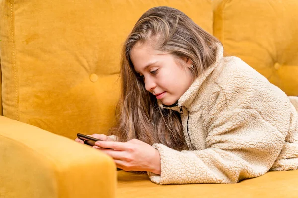 彼女の十代の女の子は黄色のソファにあり 携帯電話で再生したり 友人と通信したり 選択的フォーカス — ストック写真