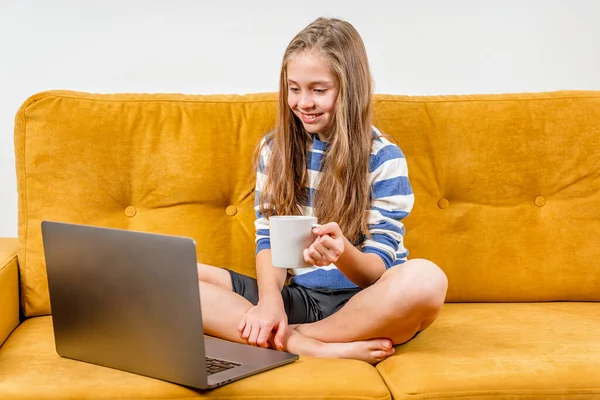 笑顔ヨーロッパの10代の女の子は黄色のソファに座っている友人や両親へのビデオ通話のためのラップトップを使用しています 遠隔オンライン教育 — ストック写真