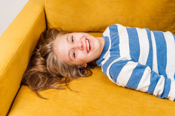 A close-up portrait of a smiling beautiful little blonde girl lying on a yellow sofa, a photo on top of her