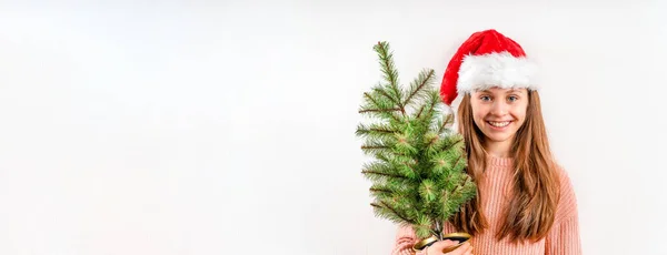 크리스마스 모자를 아름다운 금발의 소녀가 웃으며 배경에 크리스마스 트리를 있습니다 — 스톡 사진