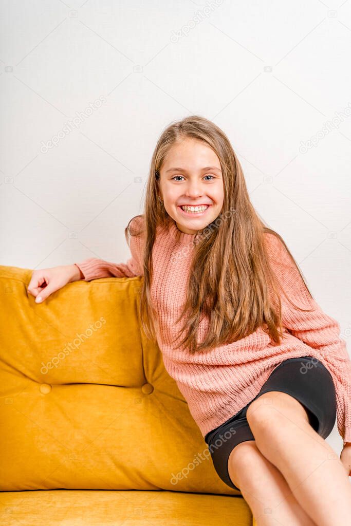 Beautiful little girl makes a face and fooling around sitting on a yellow sofa