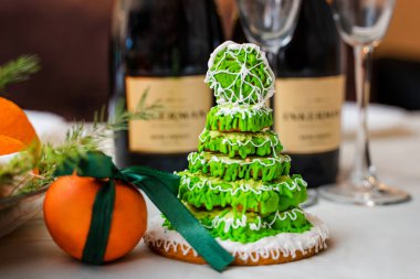 Gingerbread in the form of a Christmas tree with green glaze on a New Year's table against a background of champagne