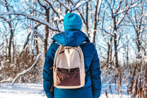 帽子を被った青年の後ろ姿と 冬の晴れた日に森の中の雪の道を歩くリュック — ストック写真