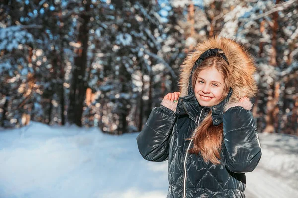 晴れた日には冬の松林の中で暖かいジャンプスーツで笑顔の女の子 — ストック写真
