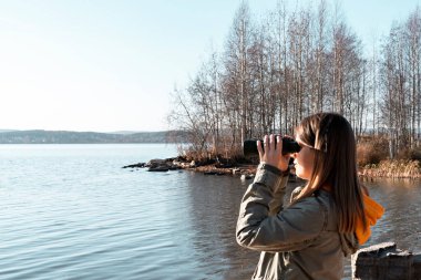 Göldeki kuşlara dürbünle bakan genç bir kadın. Kuş izleme, zooloji, ekoloji. Doğada araştırma, hayvanların gözlemlenmesi kuşbilimi sonbahar kuşları göçü