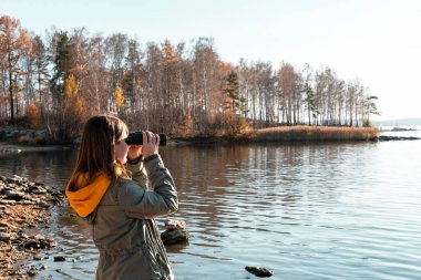 Göldeki kuşlara dürbünle bakan genç bir kadın. Kuş izleme, zooloji, ekoloji. Doğada araştırma, hayvanların gözlemlenmesi kuşbilimi sonbahar kuşları göçü