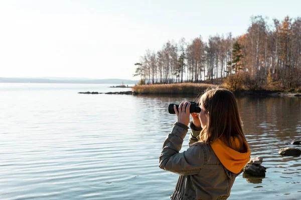 Young woman looking through binoculars at birds on the lake. Birdwatching, zoology, ecology. Research in nature, observation of animals Ornithology autumn bird migration