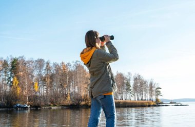 Göldeki kuşlara dürbünle bakan genç bir kadın. Kuş izleme, zooloji, ekoloji. Doğada araştırma, hayvanların gözlemlenmesi kuşbilimi sonbahar kuşları göçü