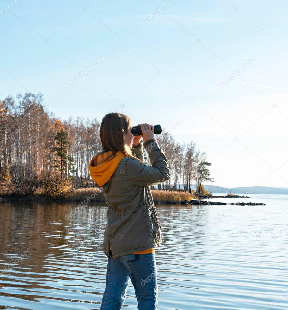 Young woman looking through binoculars at birds on the lake. Birdwatching, zoology, ecology. Research in nature, observation of animals Ornithology autumn bird migration