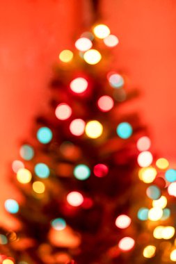 Yılbaşı arkaplanı, yılbaşı ağacı ve bulanık ışıklarla mutlu Noeller. Kırmızı arka plandaki çelenk, defocus içindeki fotokopi alanı.