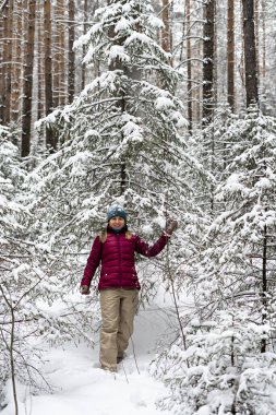 Young cheerful woman in red jacket enjoying snow falling from fir tree in winter forest, walking beauty in nature, active lifestyle, winter hiking