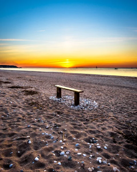 夕阳西下的沙滩上，有一条长椅 — 图库照片