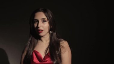 Kırmızı elbiseli esmer bir kız alacakaranlıkta şarkı söylüyor. Rüzgâr saçı savurur.