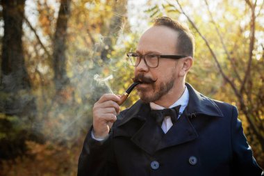 Gözlüklü şık giyinmiş bir adam, güzel bir sonbahar ormanı ve bir nehir. Yaşlı İngiliz..