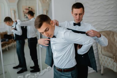 Genç bir adam damadın giyinmesine yardım ediyor. Düğün günü, neşeli bir ruh hali.