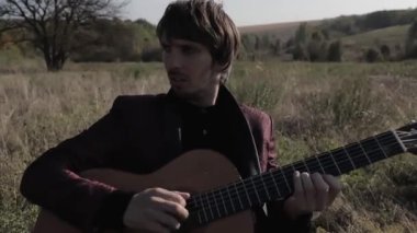 Müzisyen gün batımında bir tarlada gitar çalar. Şarap kadehli ahşap masa. Kırsal alan.