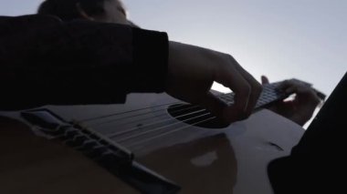Müzisyen gün batımında bir tarlada gitar çalar. Şarap kadehli ahşap masa. Kırsal alan.
