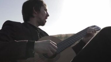 Müzisyen gün batımında bir tarlada gitar çalar. Şarap kadehli ahşap masa. Kırsal alan.