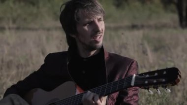 Müzisyen gün batımında bir tarlada gitar çalar. Şarap kadehli ahşap masa. Kırsal alan.