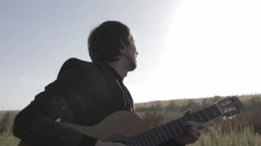 Müzisyen gün batımında bir tarlada gitar çalar. Şarap kadehli ahşap masa. Kırsal alan.