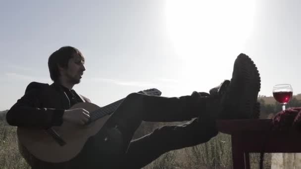 Μουσικός Παίζει Κιθάρα Ένα Χωράφι Ηλιοβασίλεμα Ξύλινο Τραπέζι Ποτήρια Κρασιού — Αρχείο Βίντεο