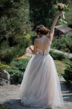 Arkadan bak. Bir bardak şampanya ve bir buket çiçekle mutlu bir gelin. Sıcak yaz günü, kozalaklı park. Arkadan bak..