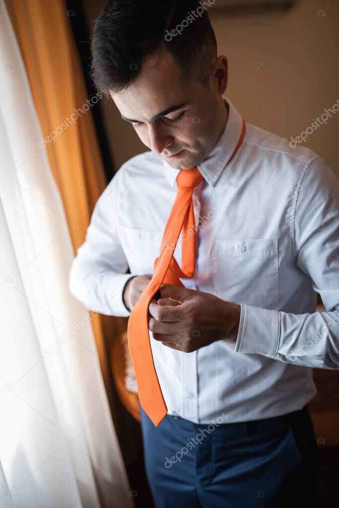Strong manly groom of Caucasian appearance, wedding day. Orange tie and blue suit. Mixed marriages