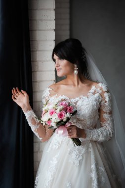 Mutlu gelin ve damat gülüyor ve öpüşüyor. Neşeli, zarif gelin pencerenin yanında. Uzun trenli uzun bir elbise..