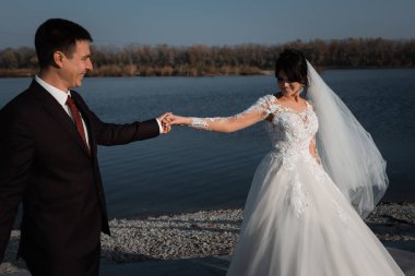 Mutlu gelin ve damat gülüyor ve öpüşüyor. Neşeli, zarif gelin pencerenin yanında. Uzun trenli uzun bir elbise..