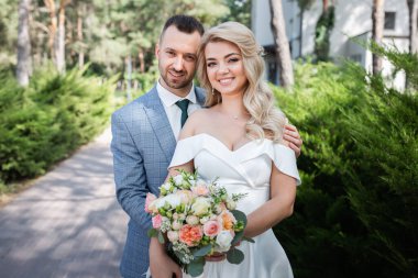 Ormanda birbirine aşık, gülümseyen bir çift el ele tutuşup sarılıyor. Güneşli bir gün, iyi bir ruh hali. Güzel bir sarışın portresi.