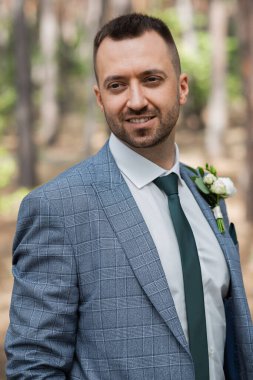 Ormanda birbirine aşık, gülümseyen bir çift el ele tutuşup sarılıyor. Güneşli bir gün, iyi bir ruh hali. Büyüleyici damat.