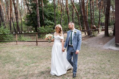 Ormanda birbirine aşık, gülümseyen bir çift el ele tutuşup sarılıyor. Güneşli bir gün, iyi bir ruh hali. Güzel bir sarışın portresi.