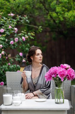 Balkonda sabahlık giymiş bir gelin. Aşık genç bir çift. Gelinin koyu renk saçları ve uzun bir peçesi var..