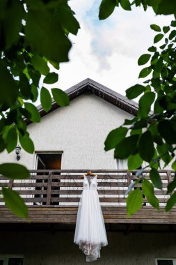 Gelinlik evin balkonunda asılı. Aşık genç bir çift. Gelinin koyu renk saçları ve uzun bir peçesi var. Gelin buketi