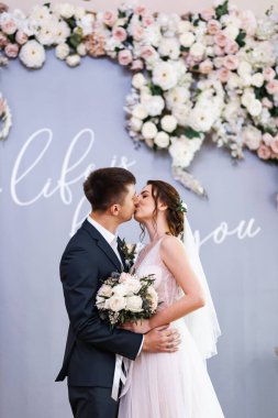 Young happy couple in love. The bride has dark hair and a long veil. Bridal bouquet. White marble staircase.