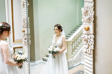 Aşık genç bir çift. Gelinin koyu renk saçları ve uzun bir peçesi var. Gelin buketi. Aynadaki yansıma. Beyaz mermer merdiven.