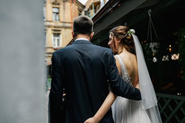 Aşık genç bir çift. Gelinin koyu renk saçları ve uzun bir peçesi var. Arkadan bak, sadece eller.