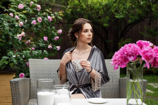 Balkonda sabahlık giymiş bir gelin. Aşık genç bir çift. Gelinin koyu renk saçları ve uzun bir peçesi var..