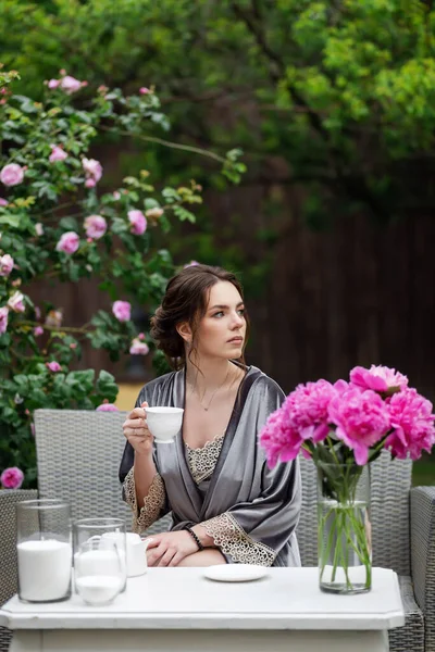 Balkonda sabahlık giymiş bir gelin. Aşık genç bir çift. Gelinin koyu renk saçları ve uzun bir peçesi var..