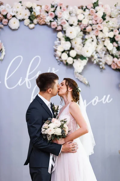 Aşık genç bir çift. Gelinin koyu renk saçları ve uzun bir peçesi var. Gelin buketi. Beyaz mermer merdiven.